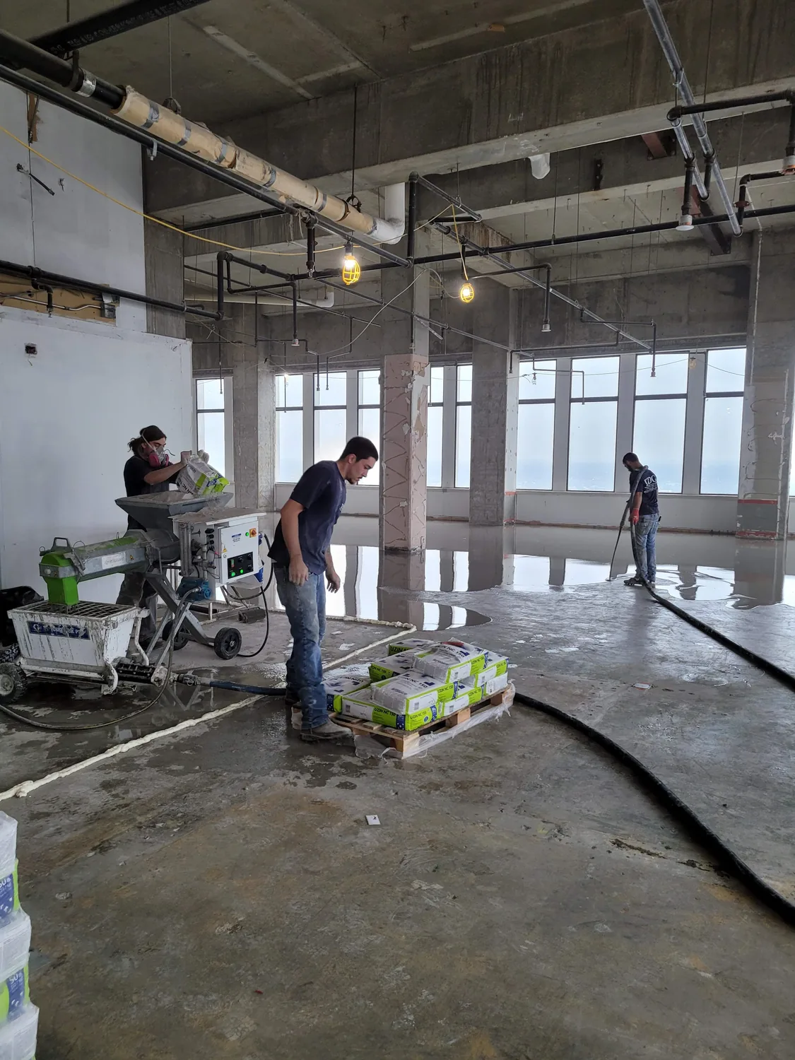 Trademark Development Group crew loading self-leveling underlayment into a mixing pump beside a pallet of bags