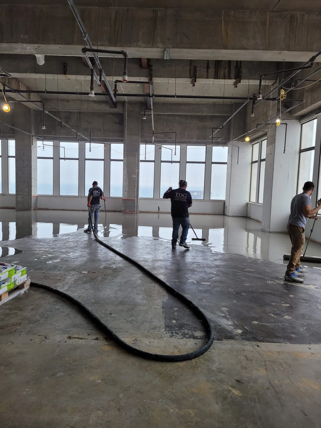 Self-leveling underlayment starting to flow across the concrete floor from the hose