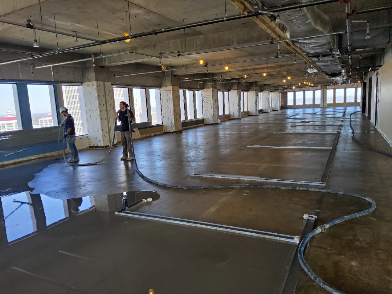 Self-leveling underlayment flowing across a high-rise office floor at 500 West, Louisville, with the downtown skyline in the windows