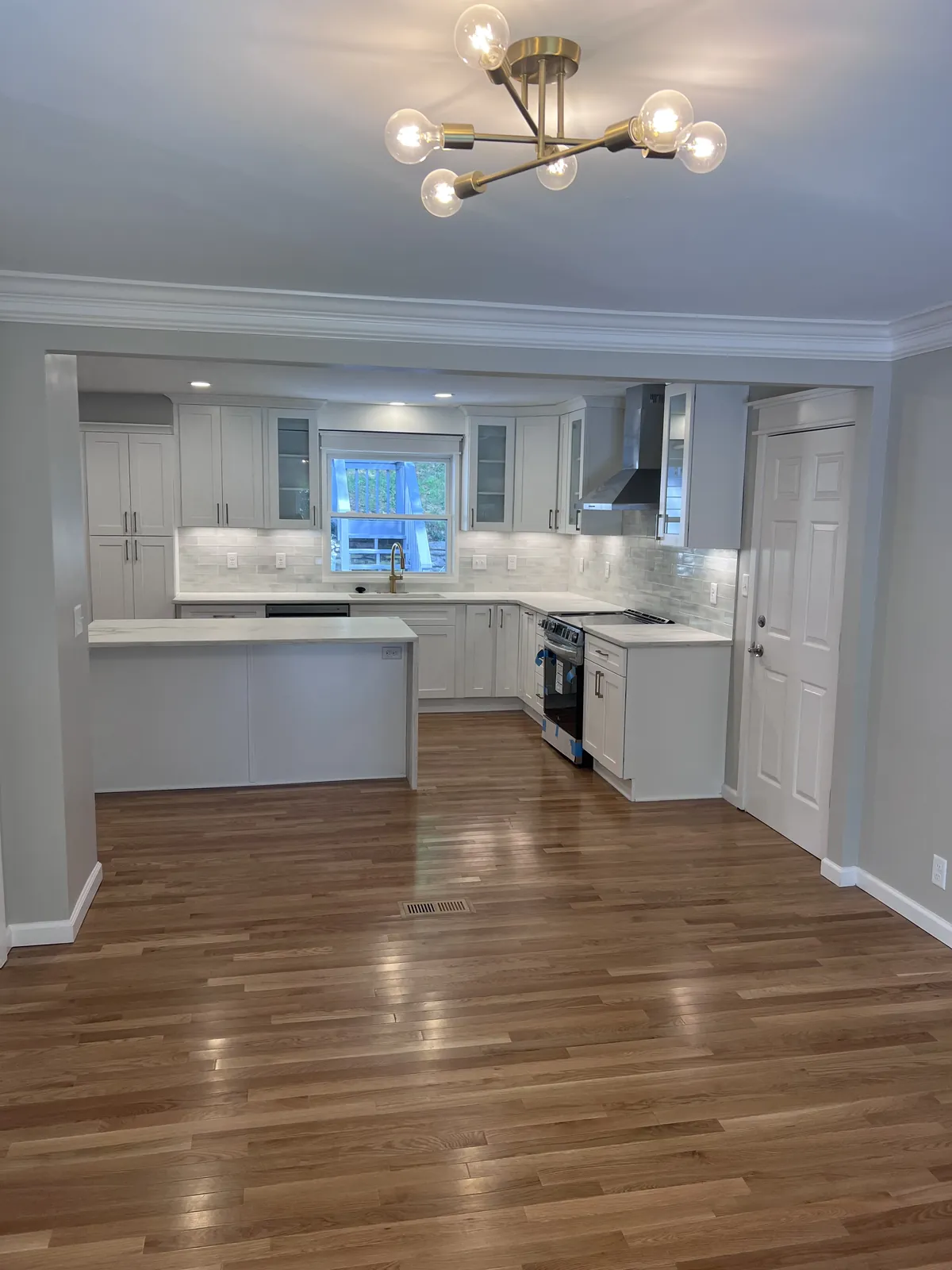 Red oak flooring in a dining room continuing into a white kitchen through a wide cased opening