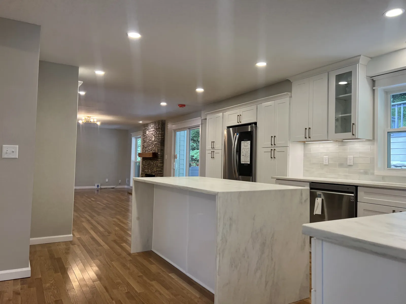 Kitchen with red oak flooring, a quartz waterfall island and white cabinetry, with the living room beyond
