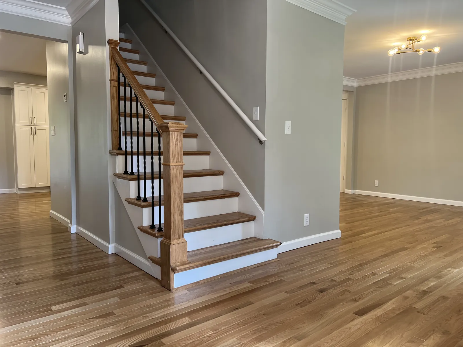 Staircase with red oak treads and newel posts matching the surrounding floor, with black iron balusters