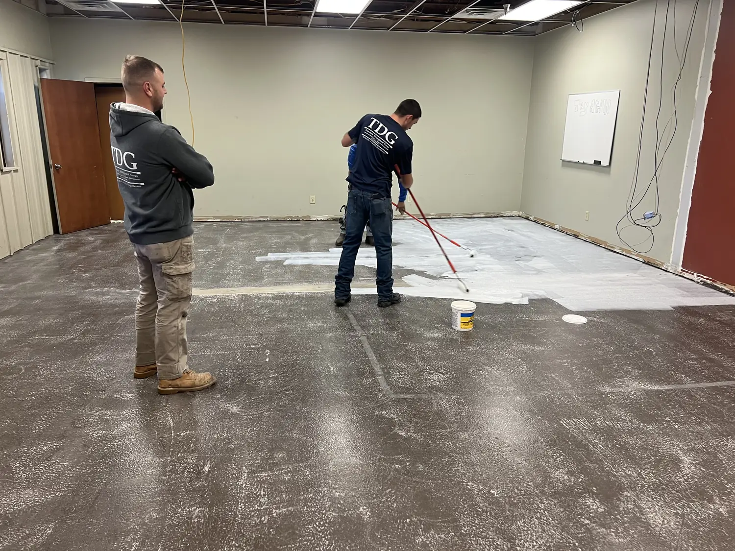 Installer rolling bonding primer, with abraded dark epoxy on one side and white primed floor on the other