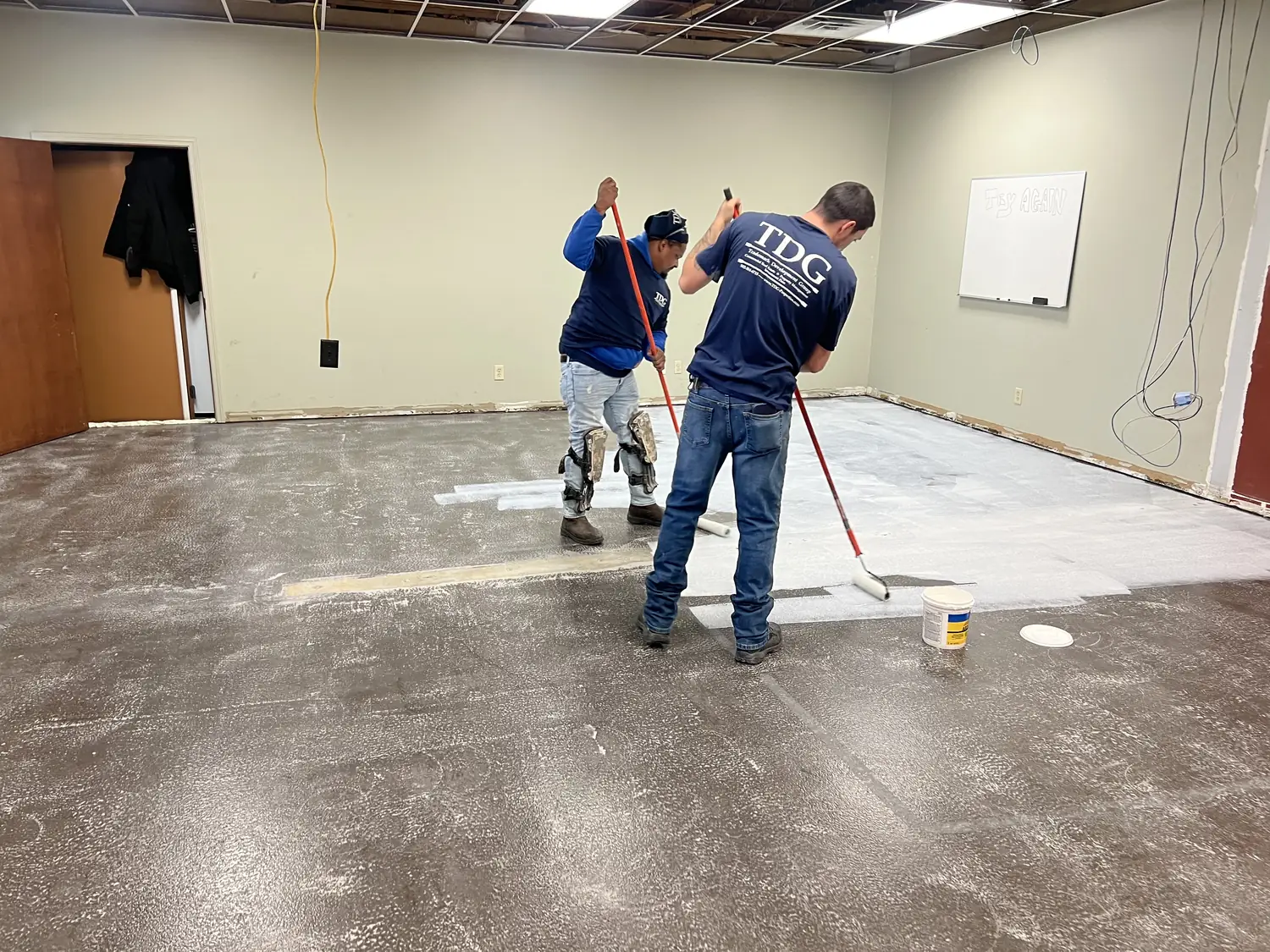 Two installers rolling primer out toward the wall line across the office floor