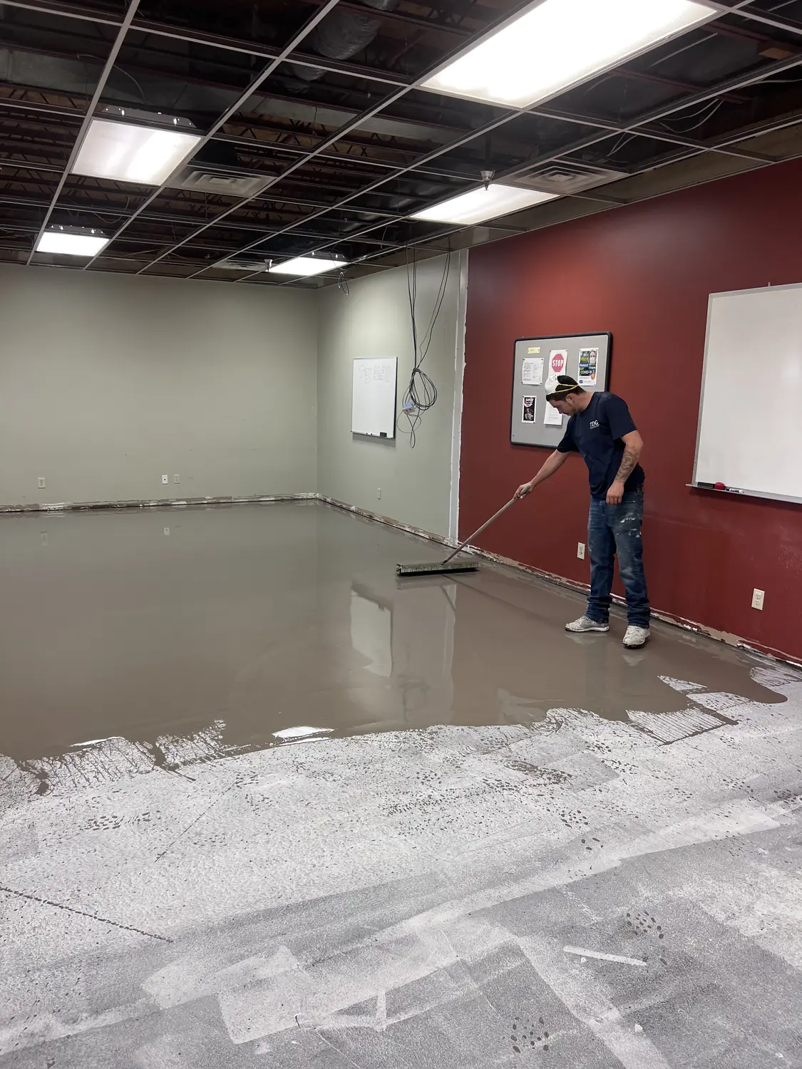 Installer working self-leveling underlayment out to depth with a gauge rake in a room with a maroon accent wall