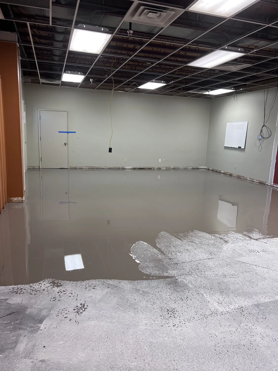 Self-leveling underlayment flowing out across an office floor with the perimeter dammed at the wall base